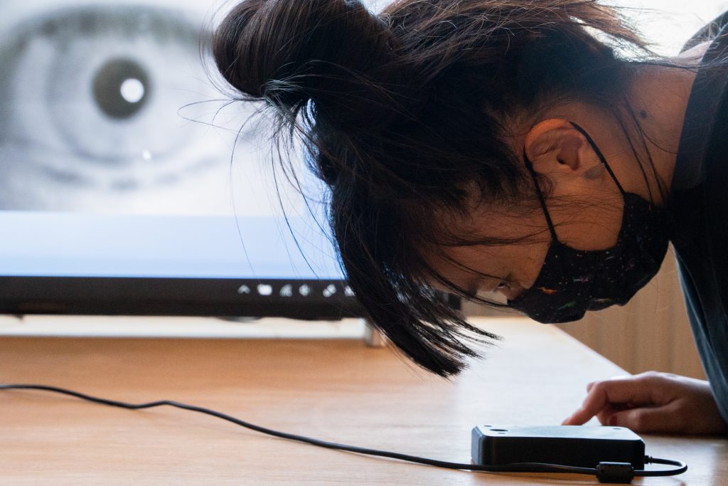 woman with face mask operating digital device with a screen showing a close up of an eye behind her