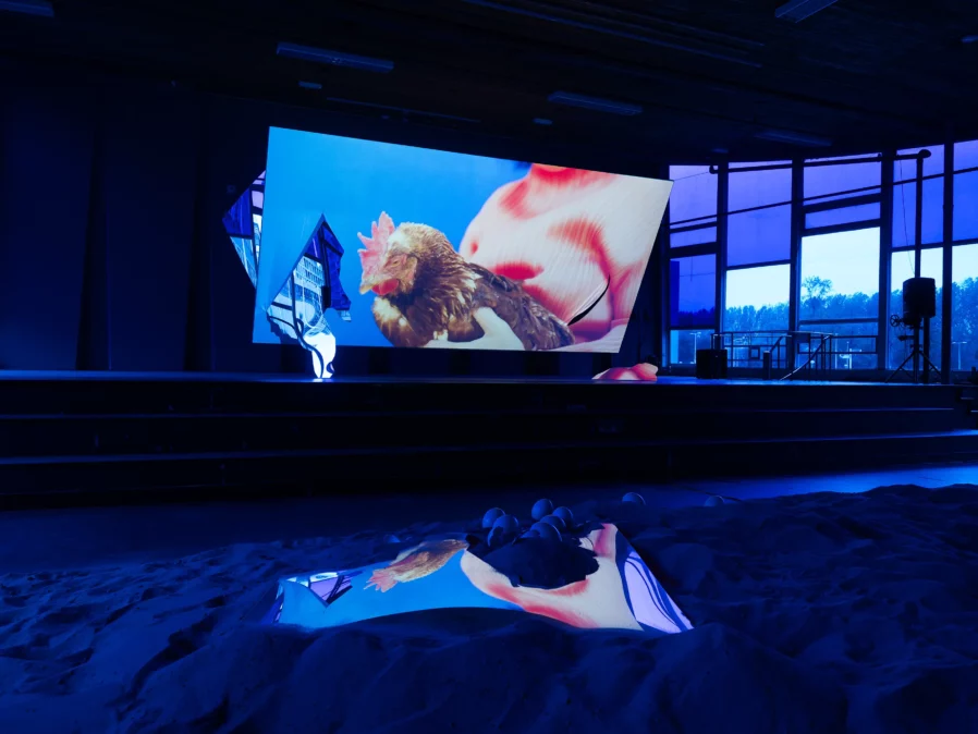 A dark blue lit room with a big screen with a chicken on